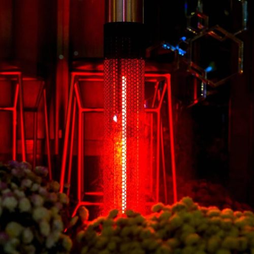 Tall red patio heater glowing beside bar stools and floral arrangements at an outdoor event